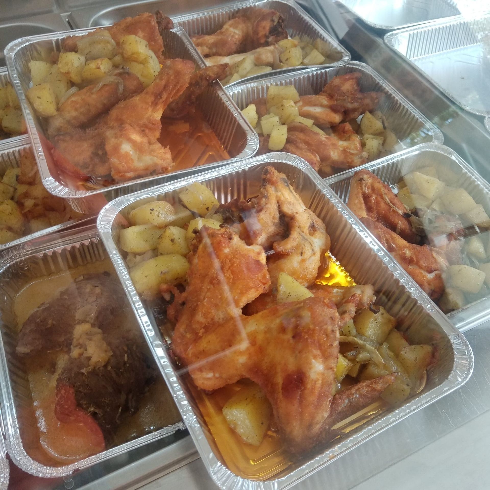 Pollo e patate in vassoi di alluminio dietro una vetrina.