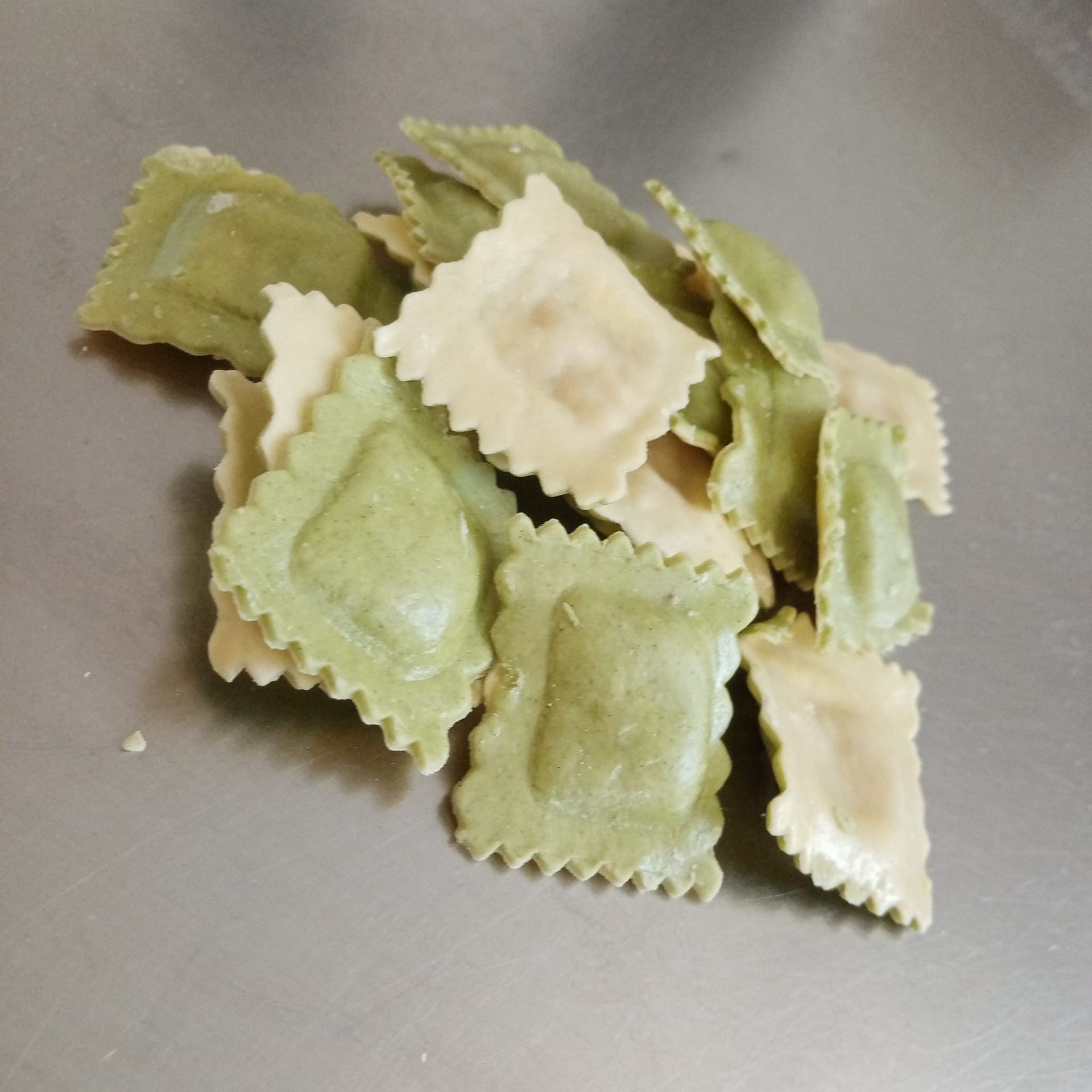 Mucchio di ravioli quadrati verdi e bianchi su una superficie argentata.