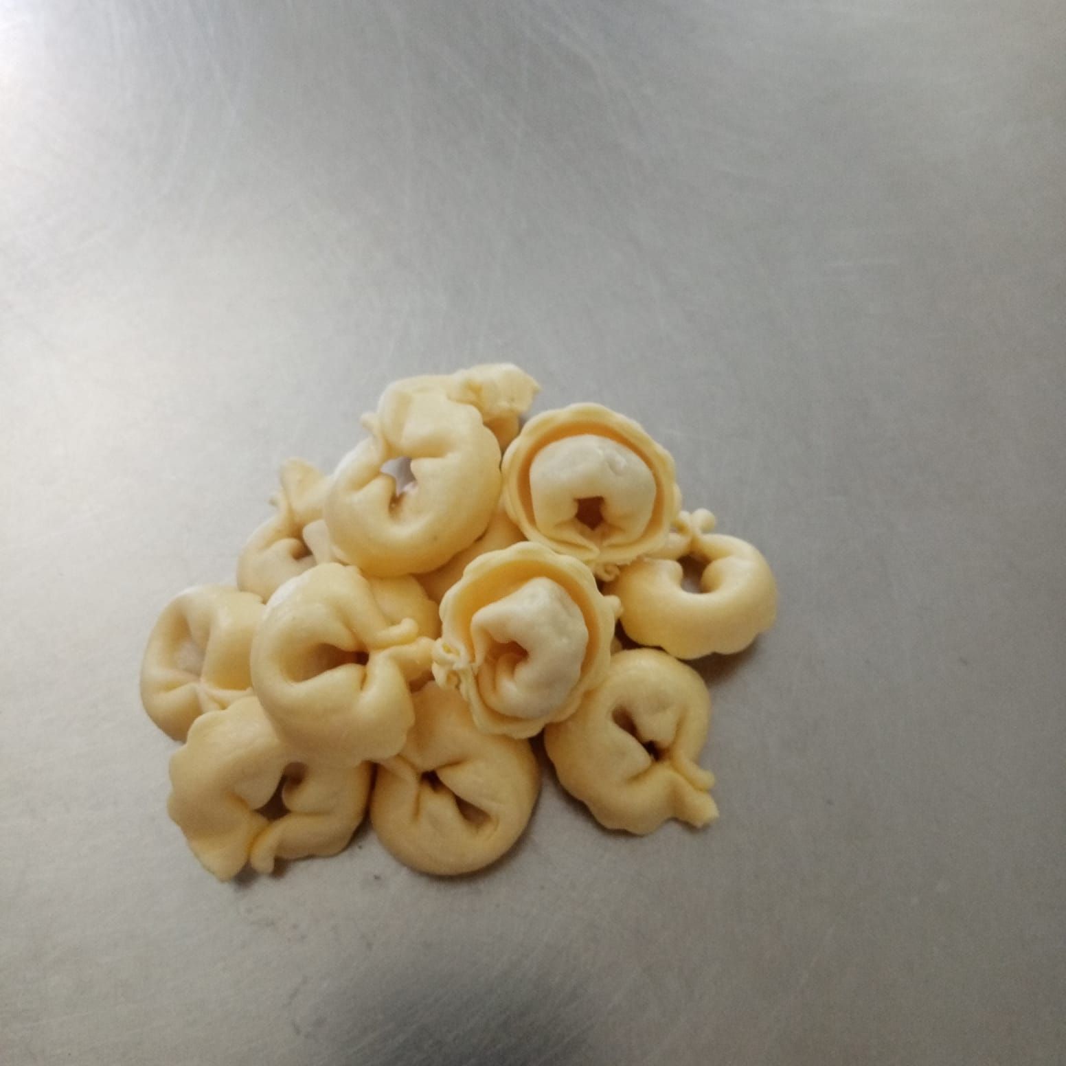 Mucchio di tortellini su una superficie metallica lucida.