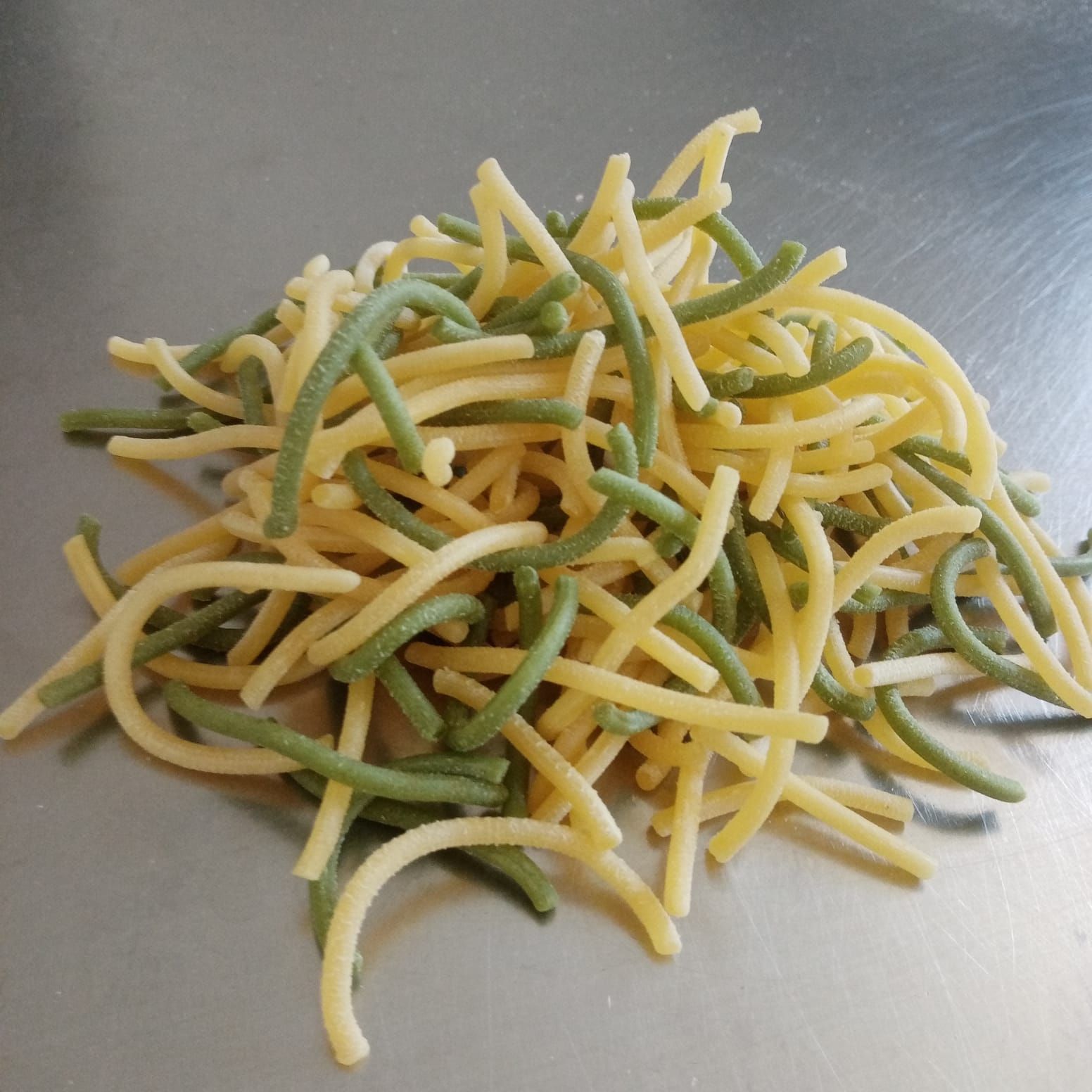 Mucchio di pasta verde e gialla, arricciata, su una superficie argentata.