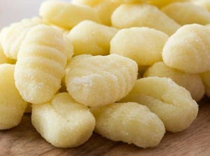 Primo piano di una pila di gnocchi giallo chiaro su una superficie di legno.