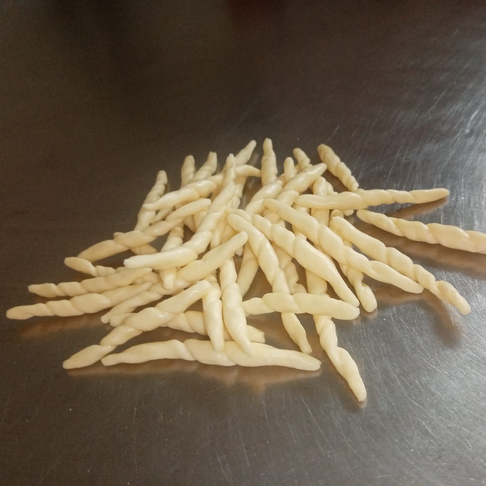 Mucchio di pasta cruda e attorcigliata su una superficie metallica lucida.
