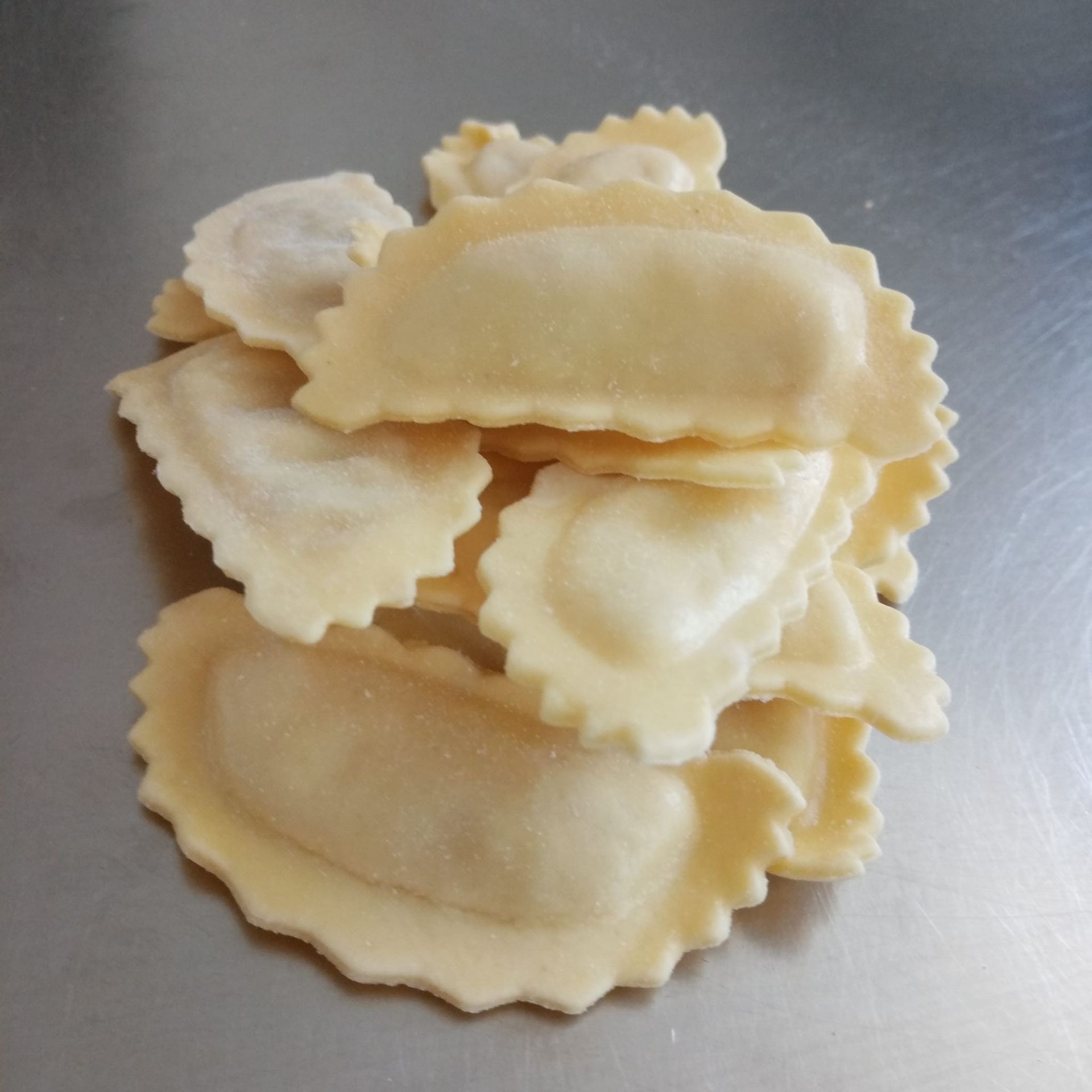Mucchio di ravioli freschi con i bordi smerlati su una superficie metallica.