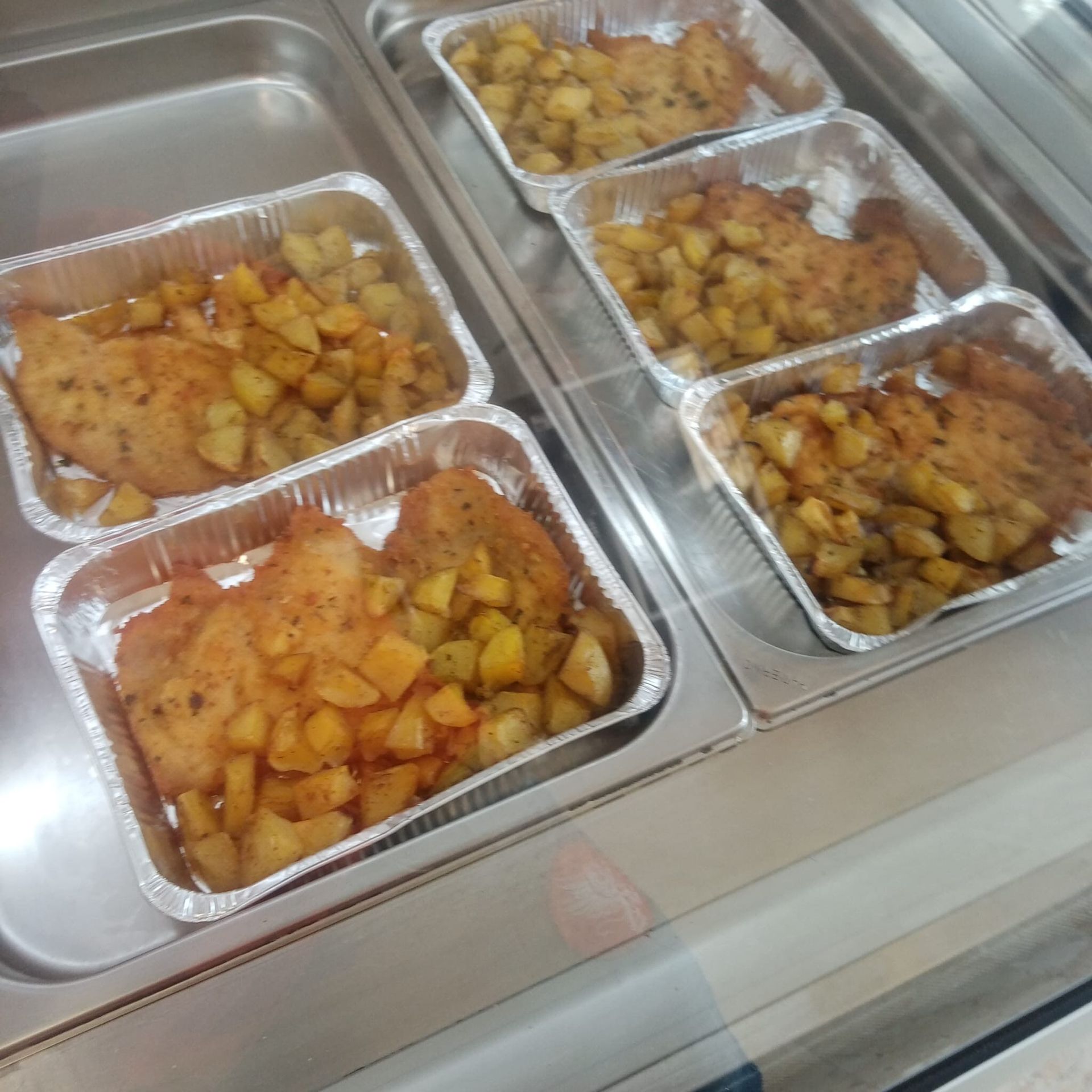 Vassoi di cotolette di pollo fritte e patate arrosto esposti su un bancone riscaldato.