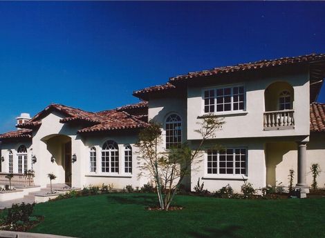 Spanish-style stucco house with red tile roof, arched windows, and a green lawn under a blue sky
