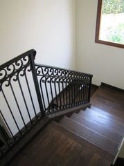 Dark wooden staircase with black wrought-iron railing beside a window and white wall
