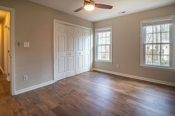 Empty beige bedroom with hardwood floor, ceiling fan, closet doors, and two windows.