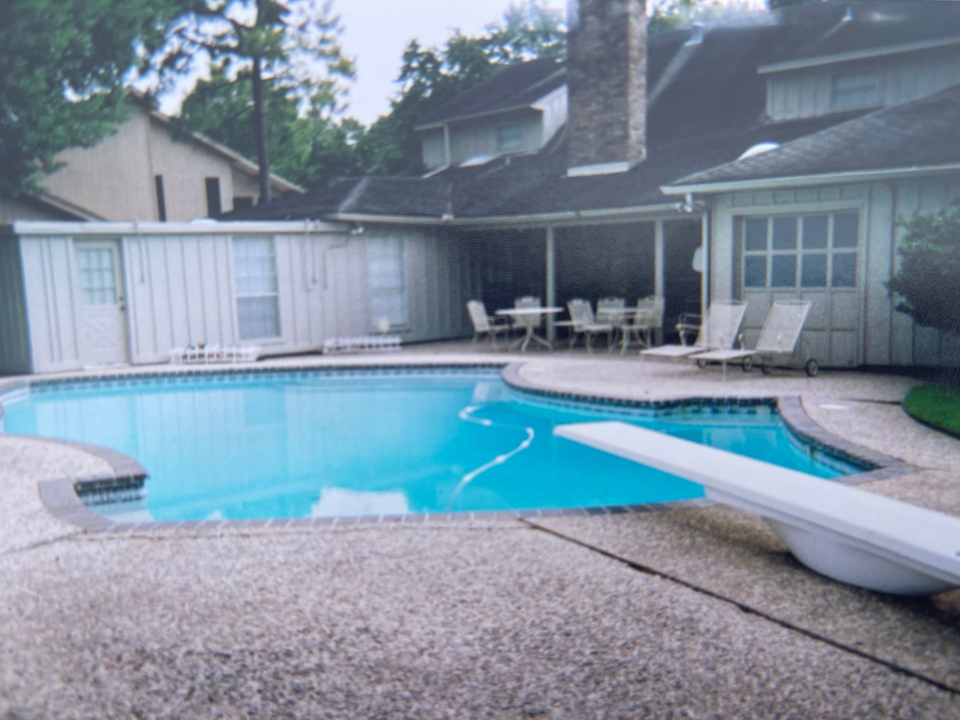 A large swimming pool with a diving board in front of a house