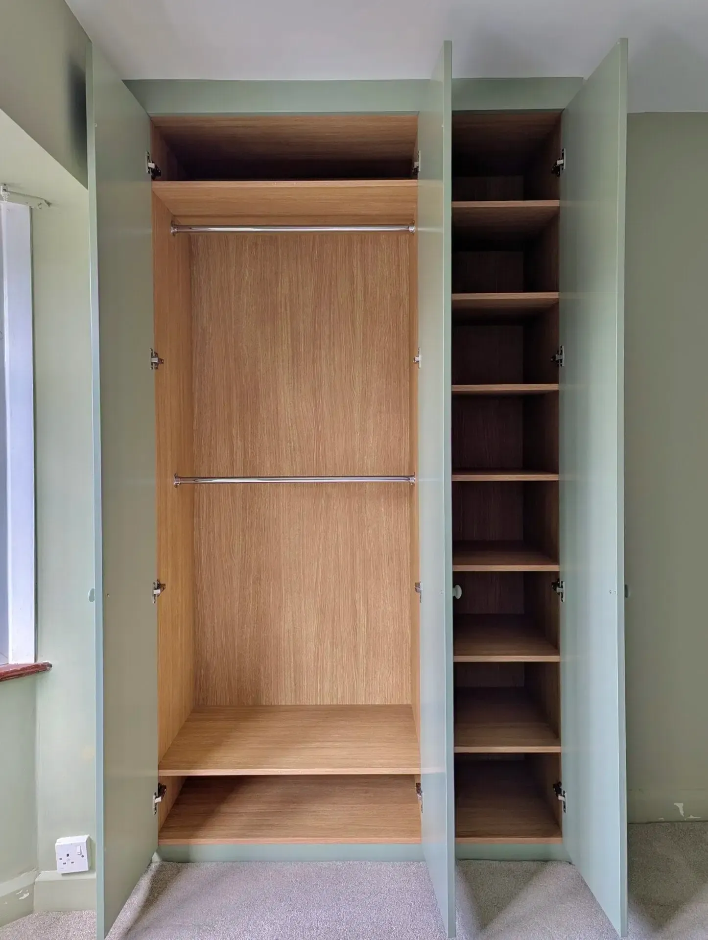 Open, empty closet with hanging rods, shelves, and light green doors and walls.