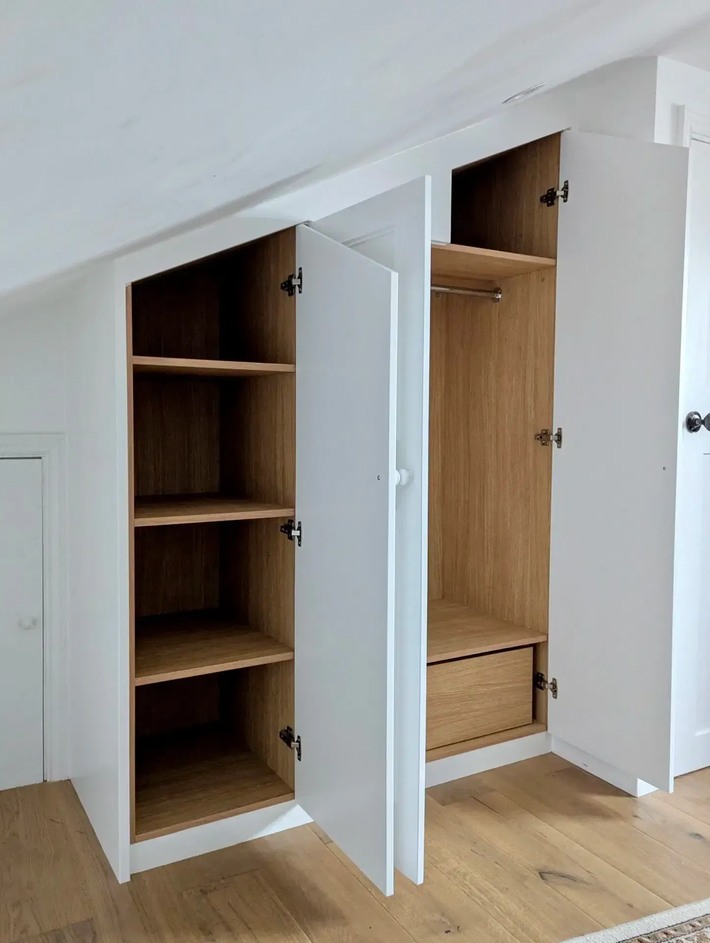 White built-in closet with open doors, featuring shelves and hanging rod against a slanted ceiling.
