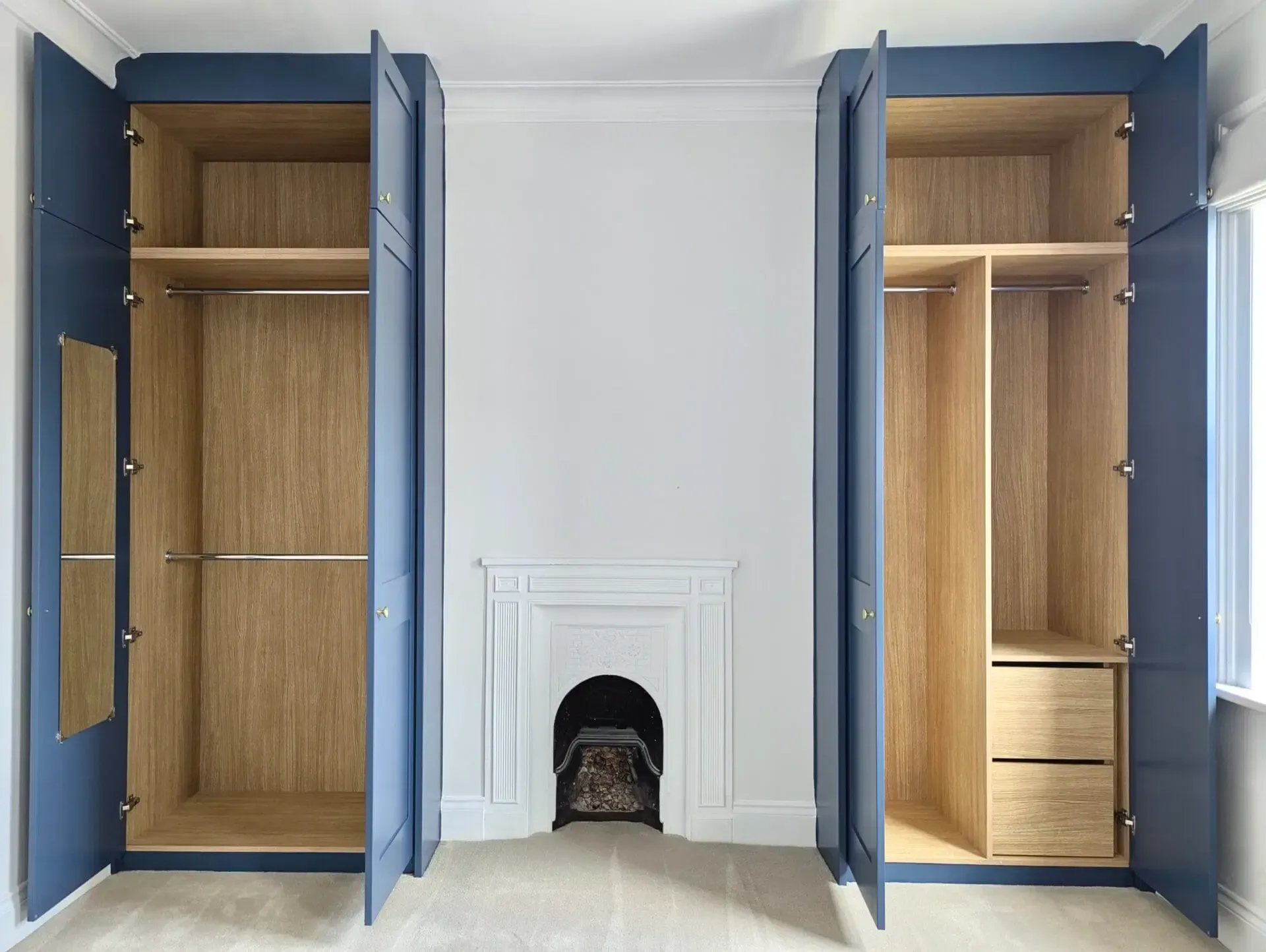 Blue built-in wardrobes flank a small fireplace. One has a mirror, the other drawers. Both have light wood interiors.