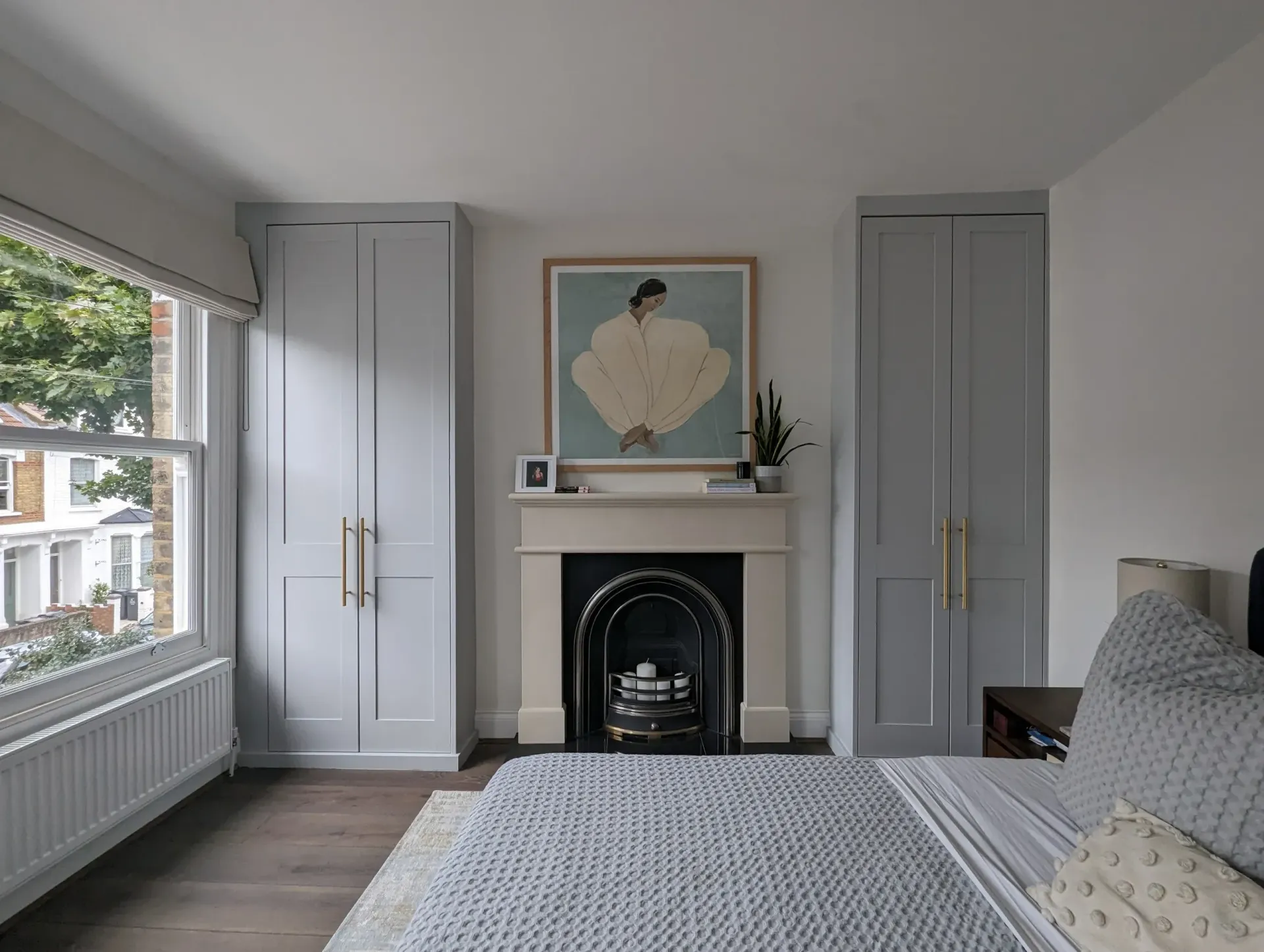 Bedroom with fireplace, two blue closets, artwork, and window overlooking trees.