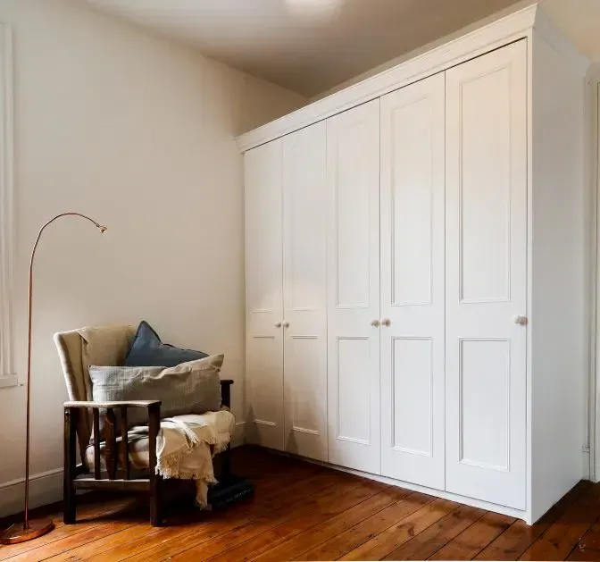 White closet with six doors beside a wooden chair, floor, and floor lamp in a room.