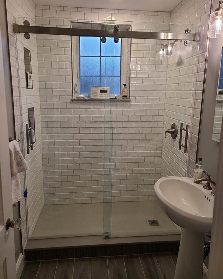 A bathroom with white brick walls , a sink , and a walk in shower.