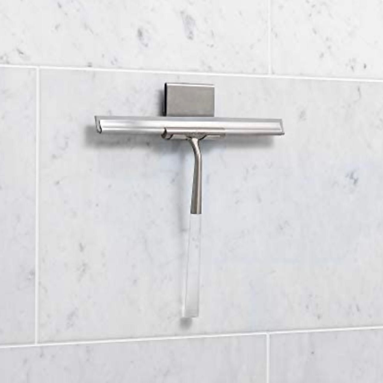 A stainless steel shower squeegee is hanging on a tiled wall.