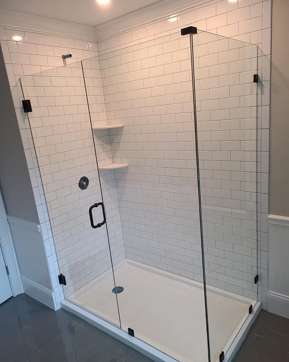 A bathroom with white tiles and a walk in shower with a glass door.