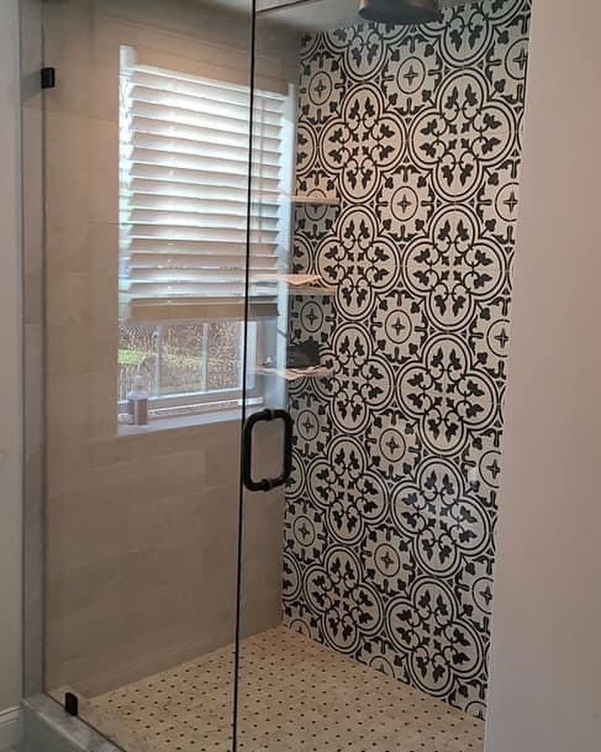 A shower with a black and white tile wall and a window.