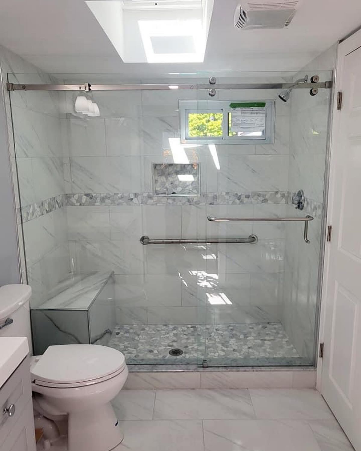 A bathroom with a toilet , sink , shower and skylight.