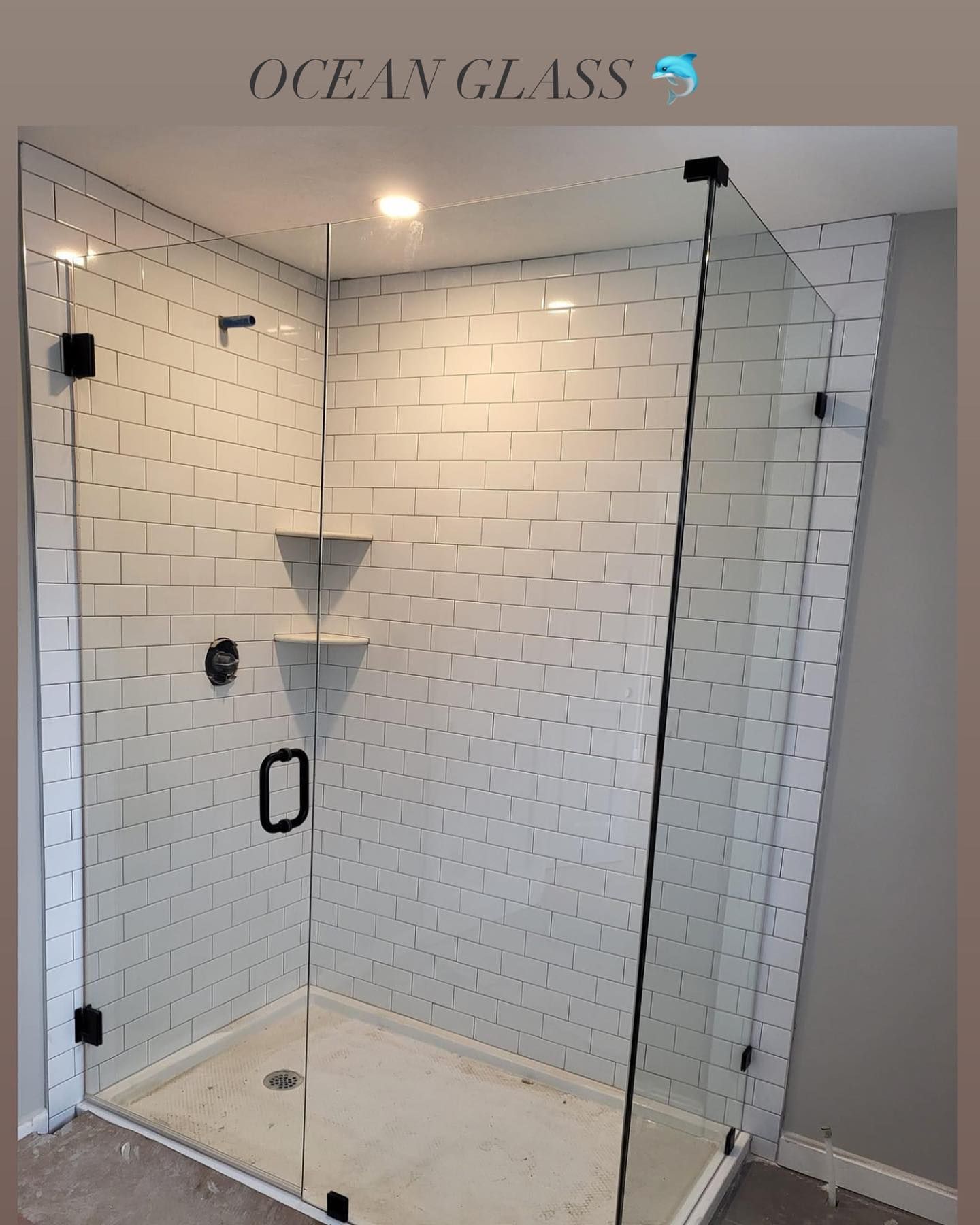 A bathroom with white tiles and a walk in shower with a glass door.
