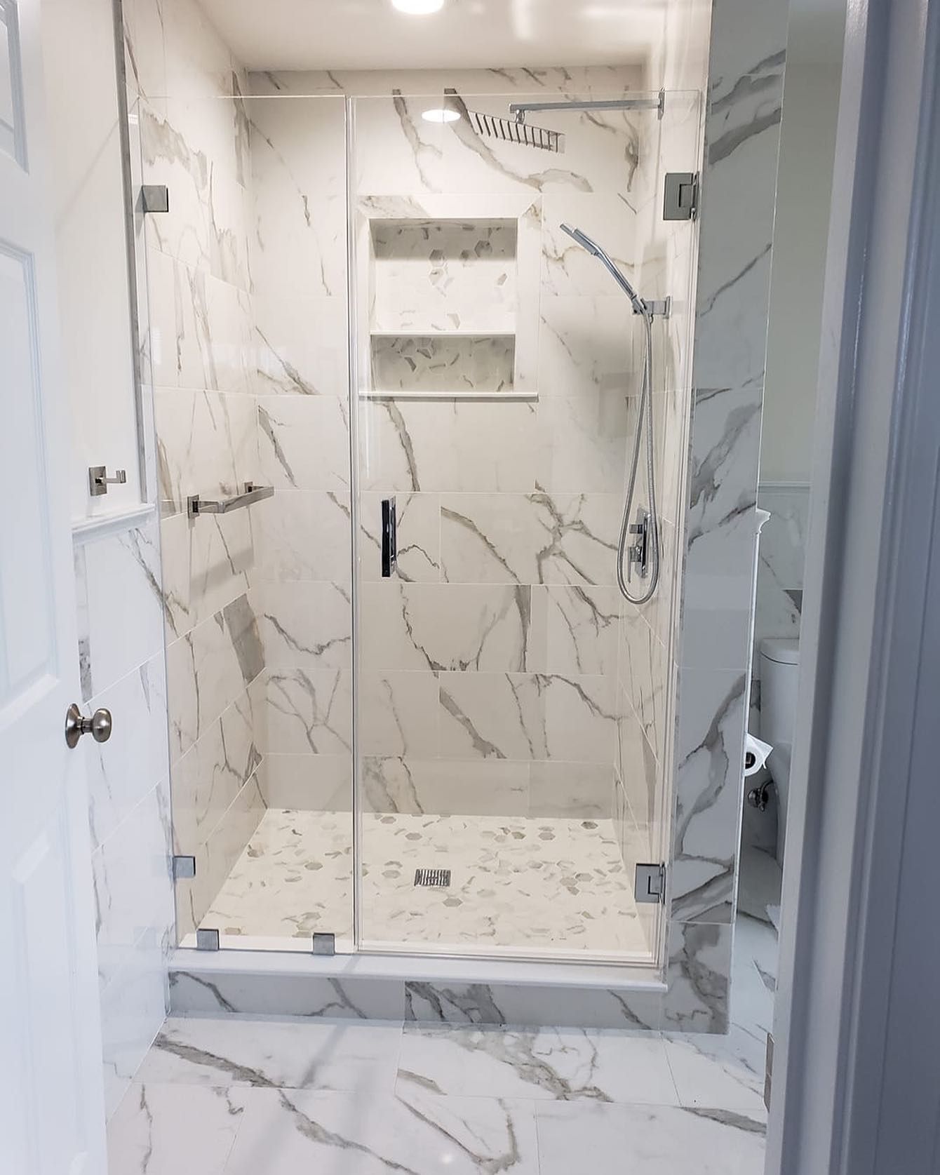 A bathroom with marble tiles and a glass shower door