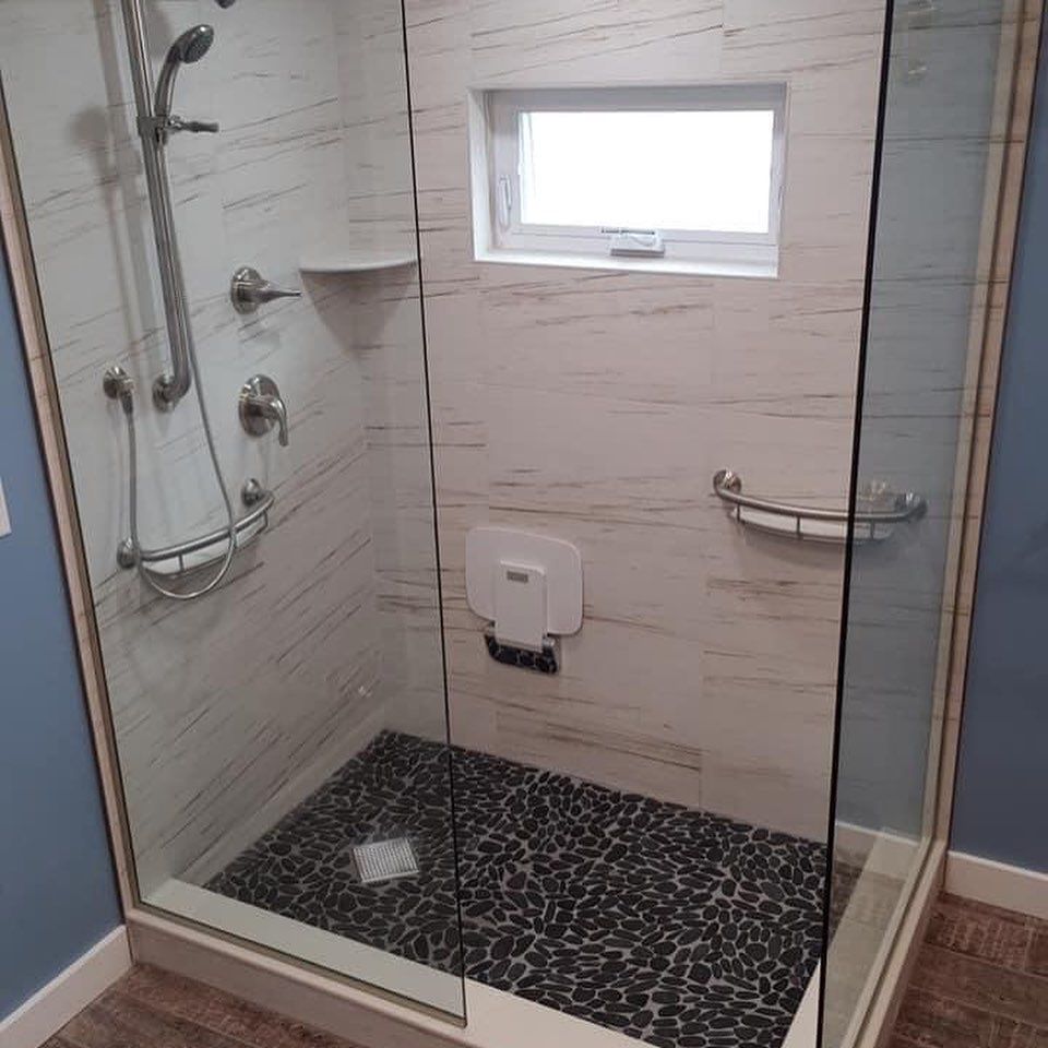 A bathroom with a walk in shower with a glass door and a window.