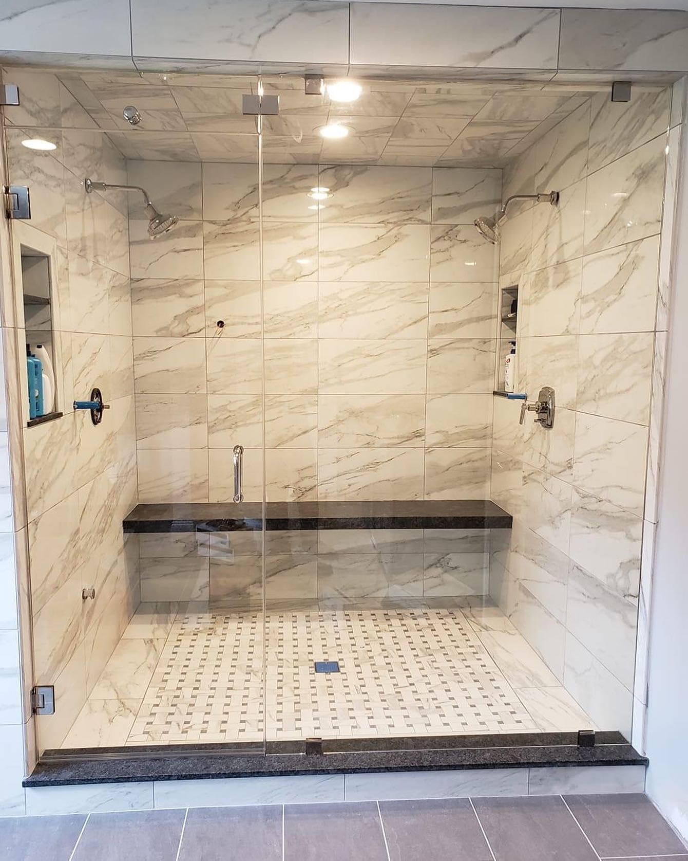 A bathroom with a walk in shower with a glass door and a bench.