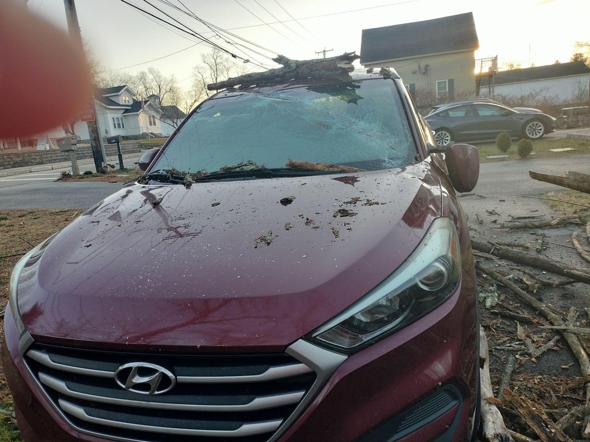 A red car with a broken windshield is parked on the side of the road.