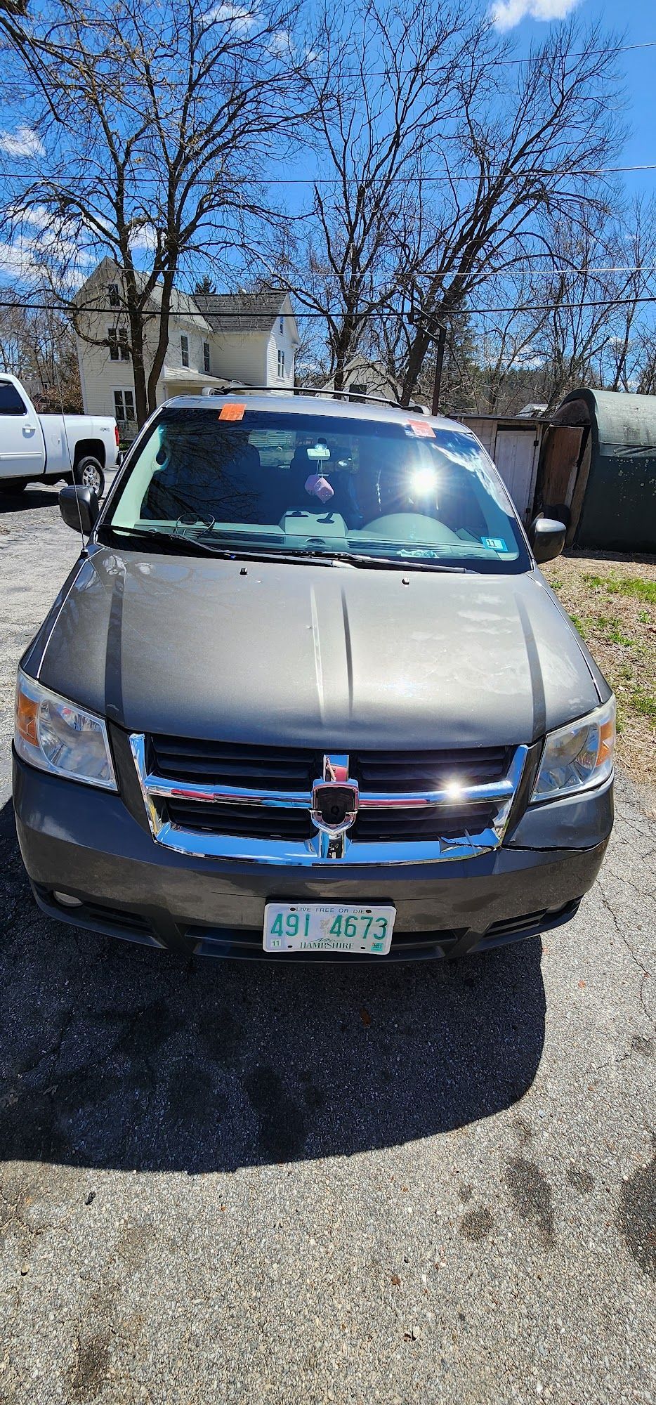 A gray minivan is parked in a gravel lot in front of a house.