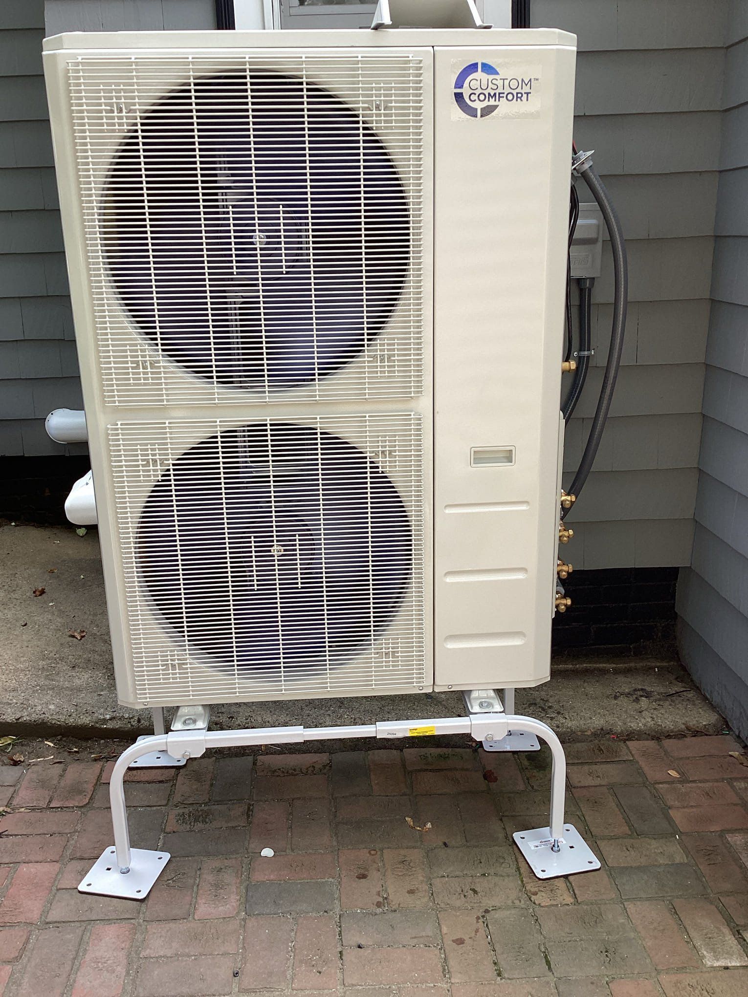 Exterior air conditioning unit on a white metal stand, against a siding wall.