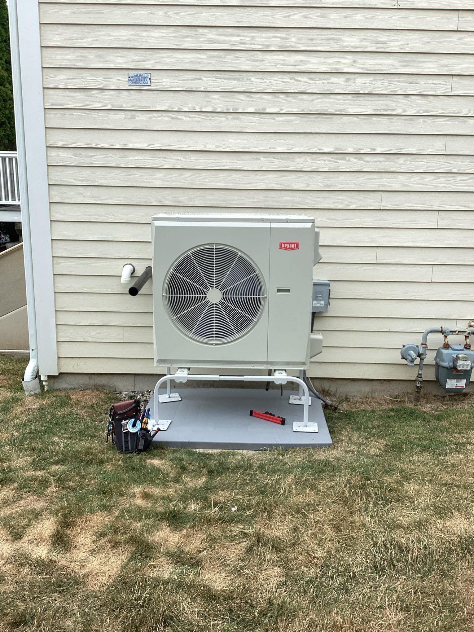 Exterior air conditioning unit on a concrete pad, next to a home's siding and gas meter.