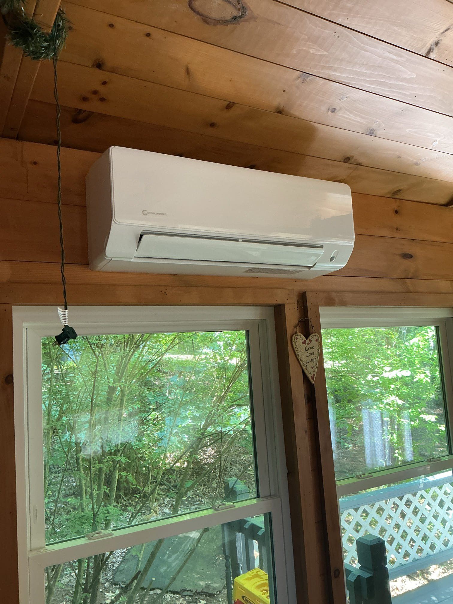 White ductless air conditioner mounted on wooden wall above windows.