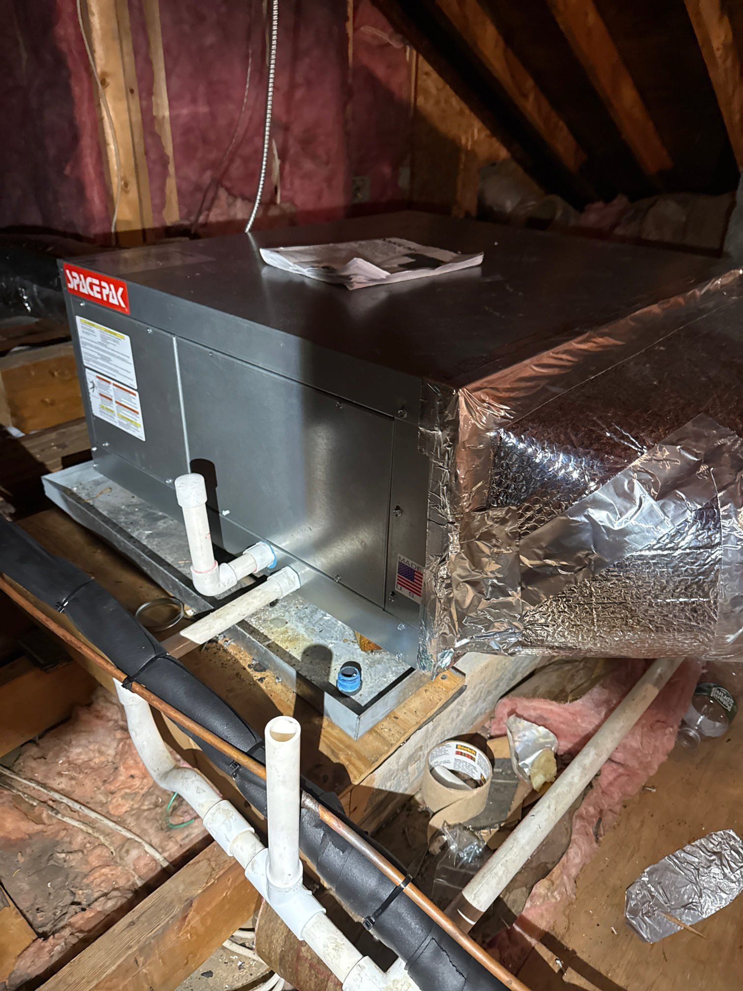 HVAC unit in an attic with ductwork, piping, insulation, and wooden beams.