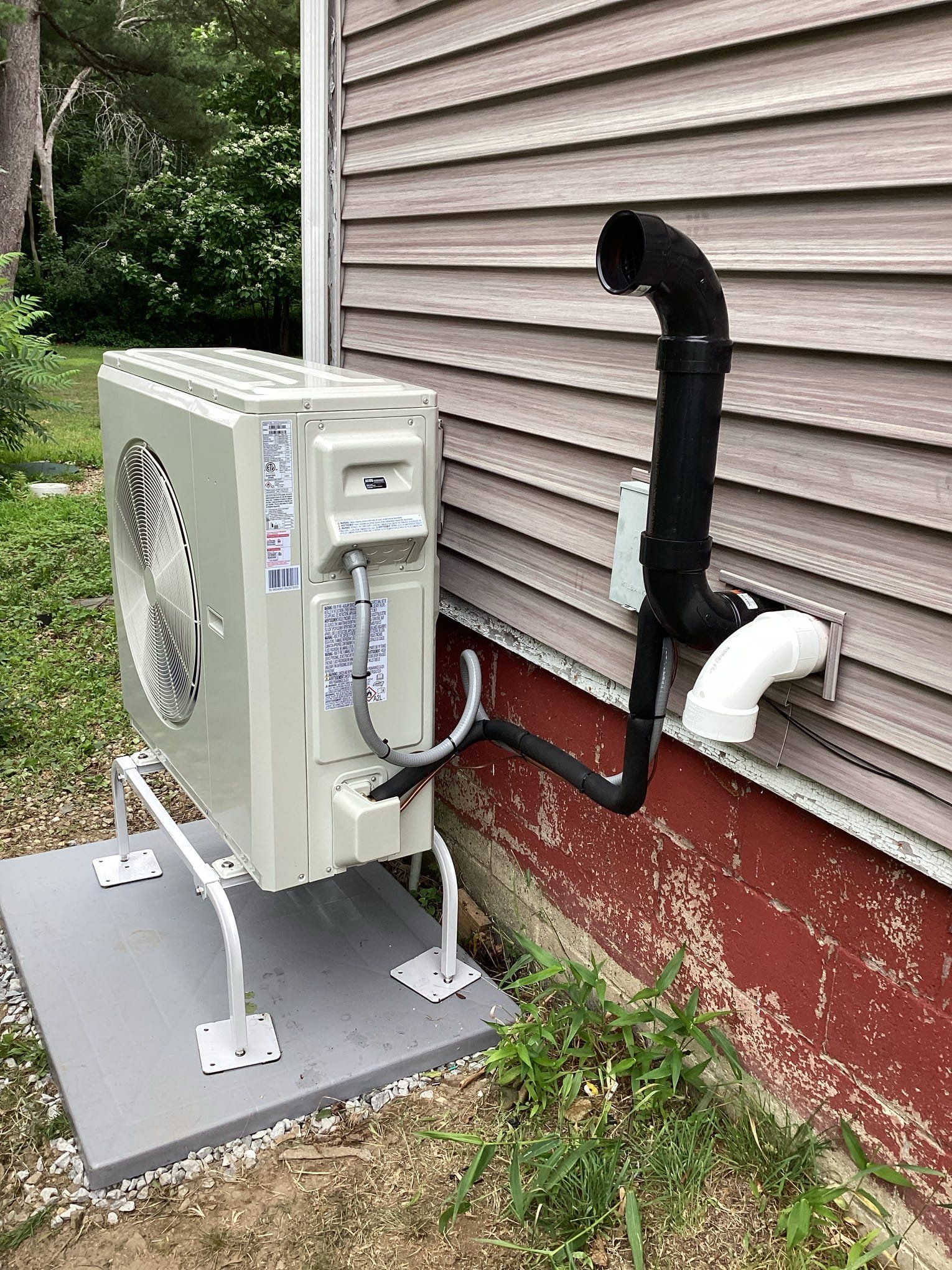 Heat pump unit with black and white piping attached to a building's exterior wall.
