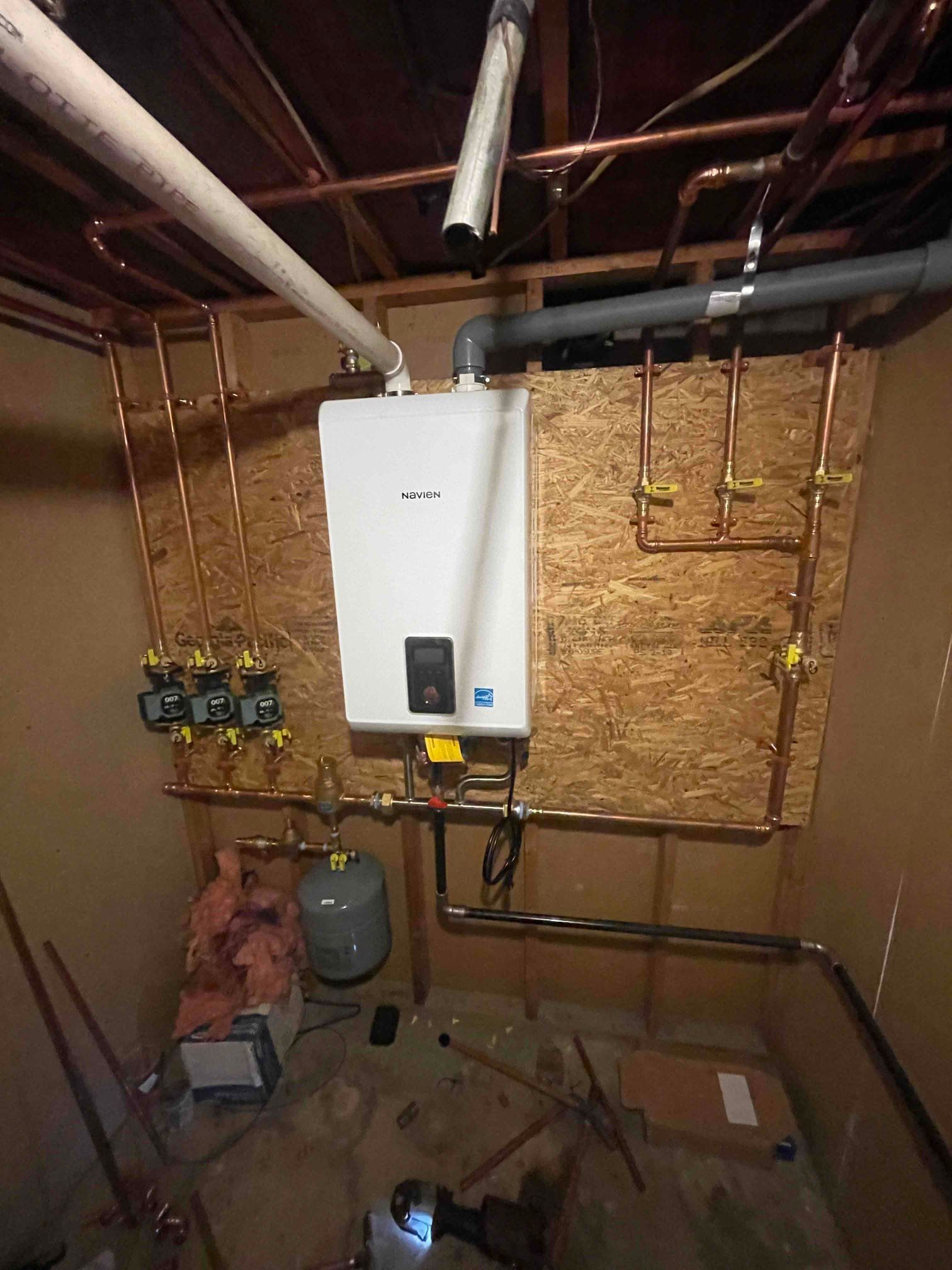 White tankless water heater installed in a utility room with copper pipes and various plumbing components.