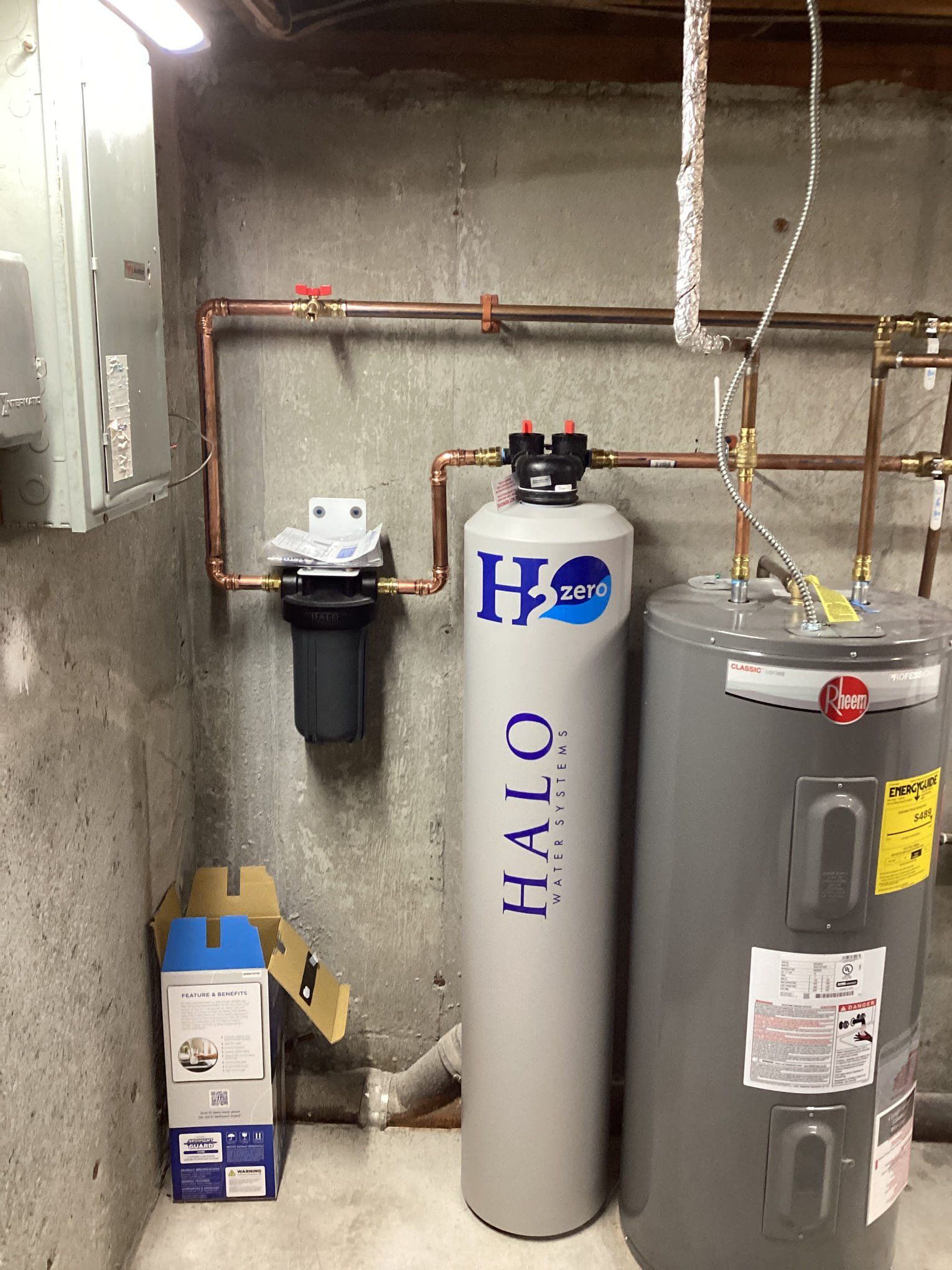 Water filtration system and water heater in a utility room with copper piping and concrete walls.