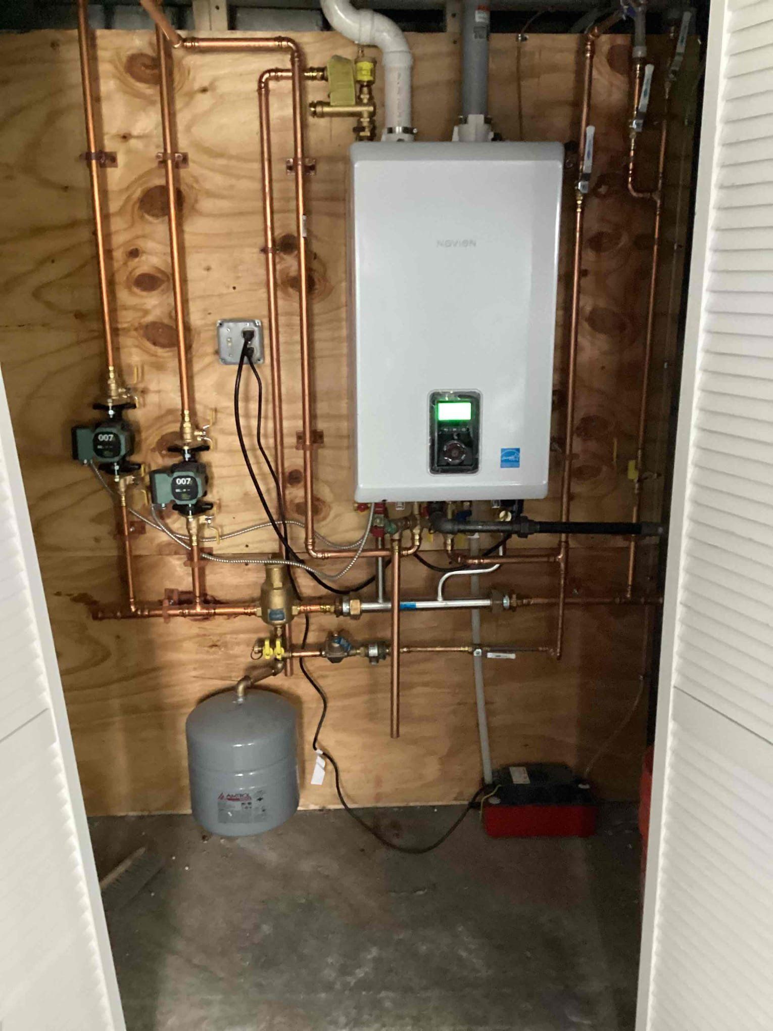 Copper pipes and a white water heater installed on a wooden wall in a utility room.