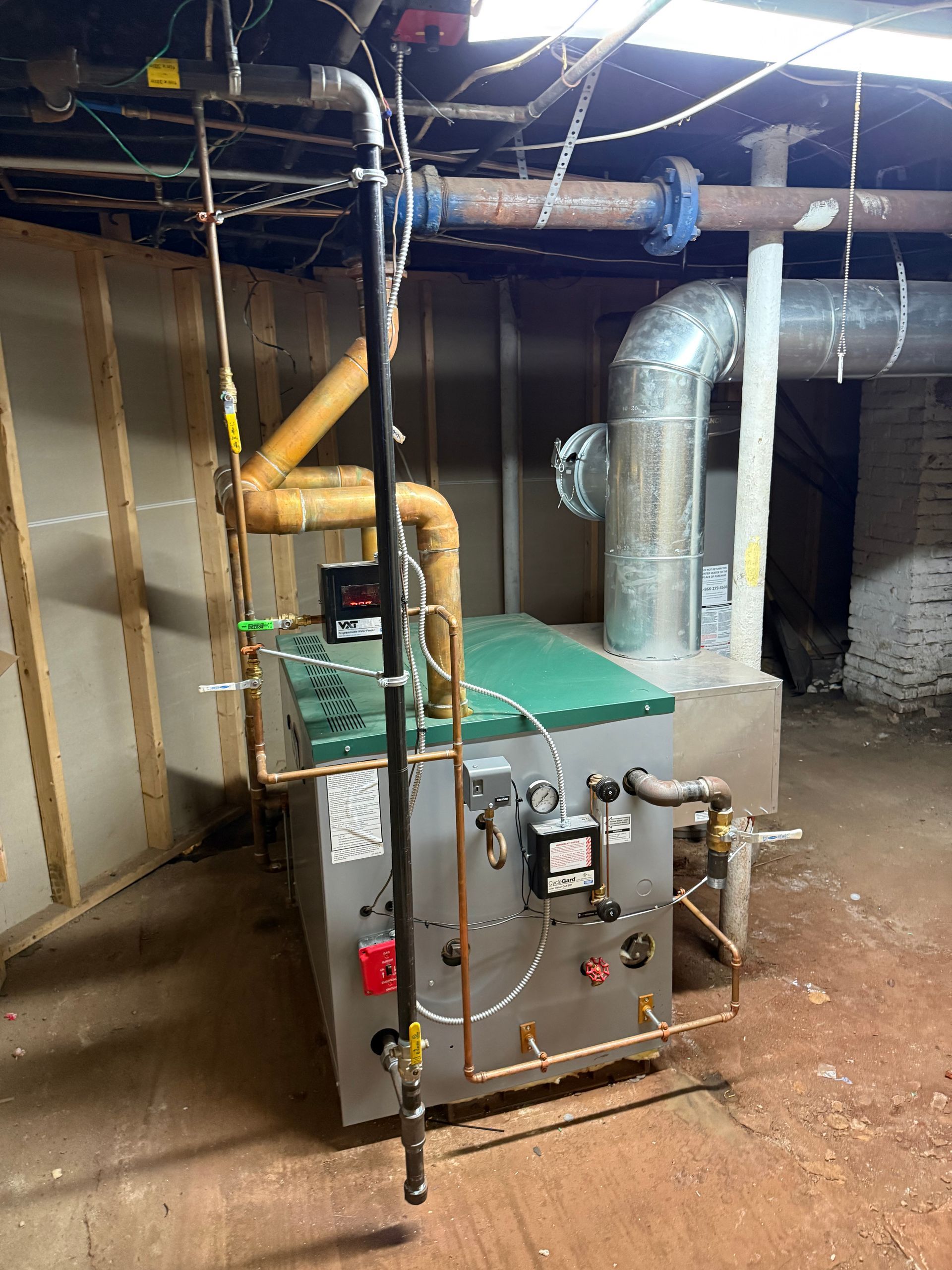 A residential furnace in a basement. It is gray with copper piping and a green top.