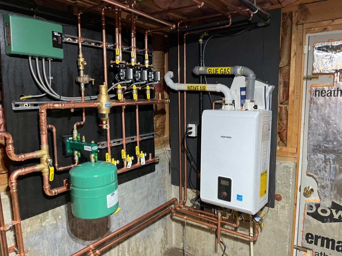 Copper pipes and heating equipment installed on a basement wall. Green and white components are visible.