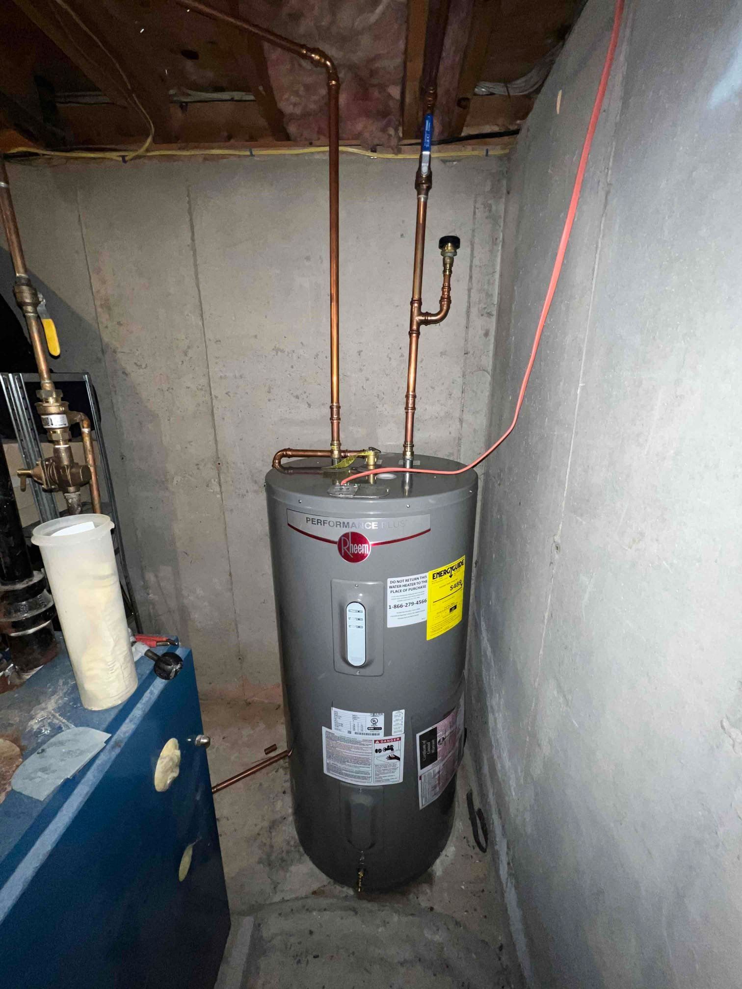 A water heater in a basement with copper pipes attached to it.