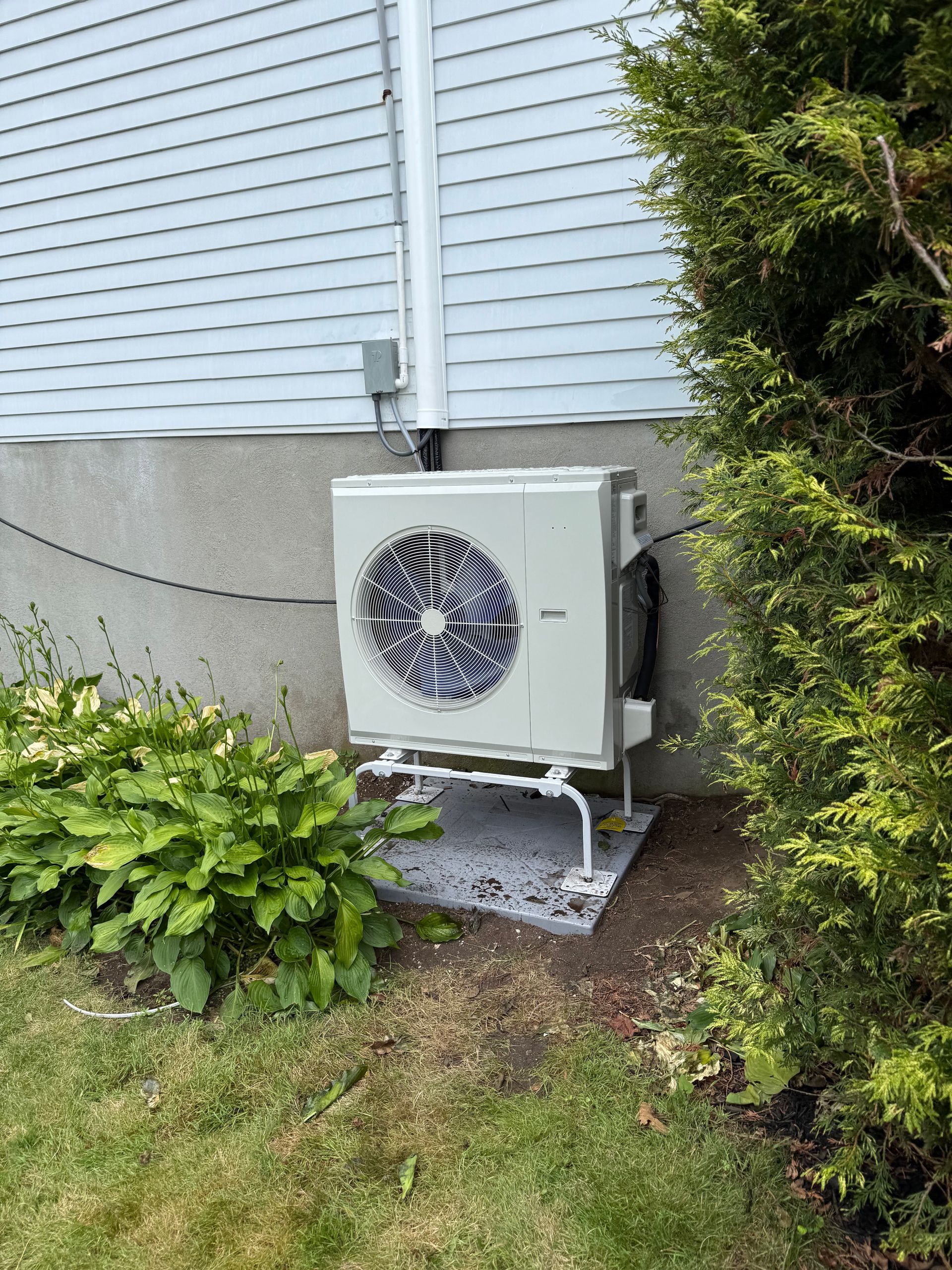 An outdoor HVAC unit next to a house with shrubs and a bush.