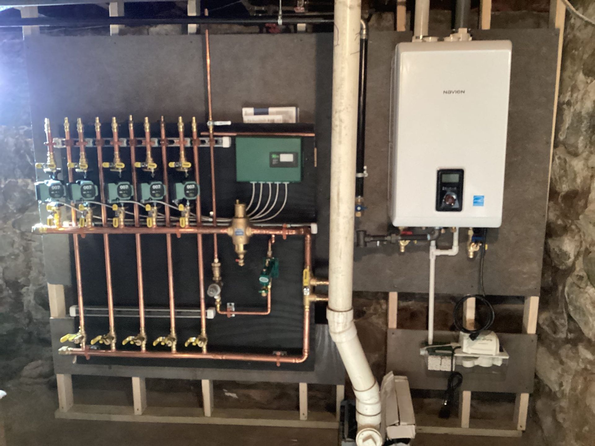 A wall-mounted heating system with copper pipes and a white water heater in a basement.