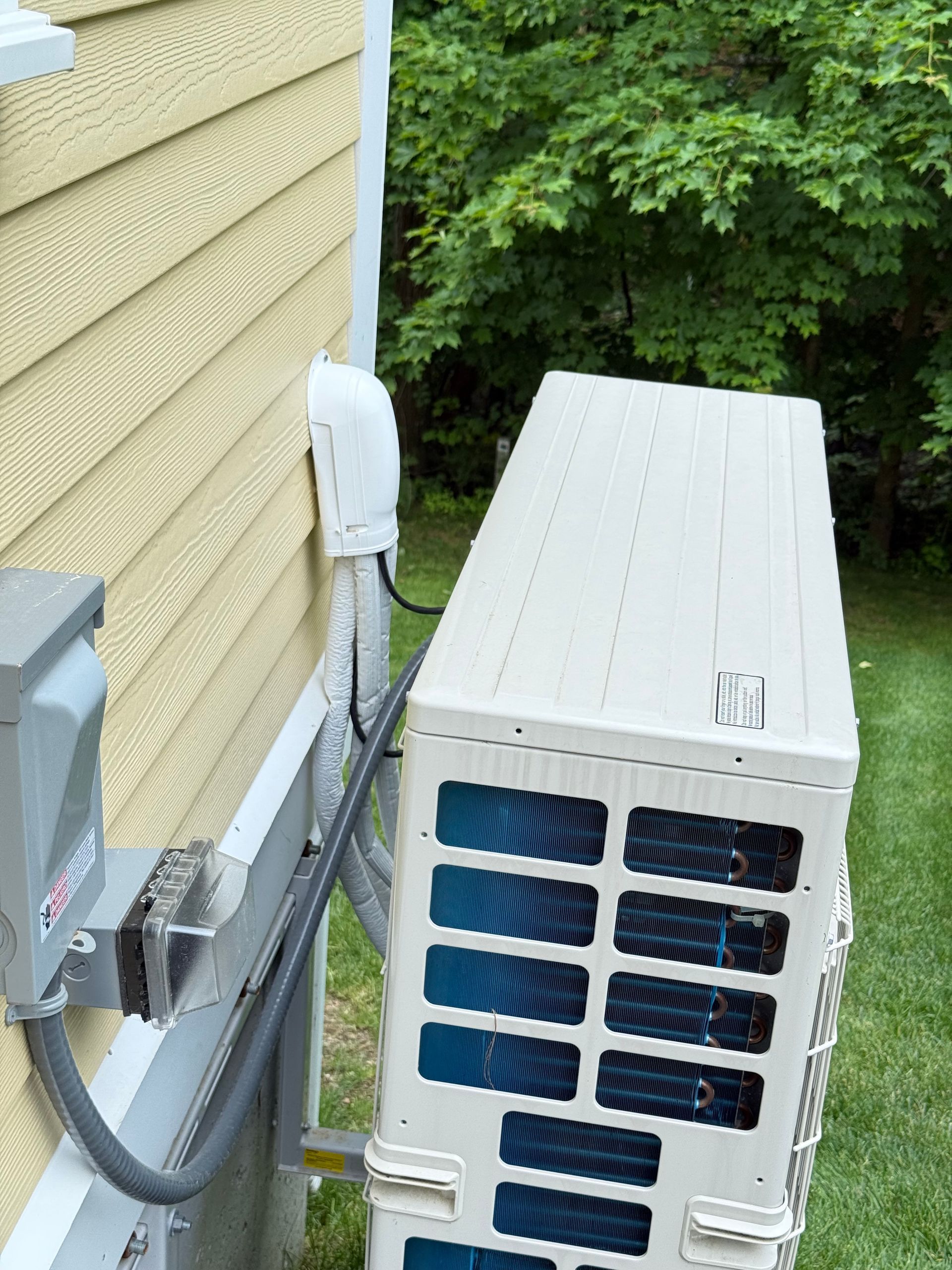 Outdoor HVAC unit mounted on a beige wall, with electrical box and conduit.