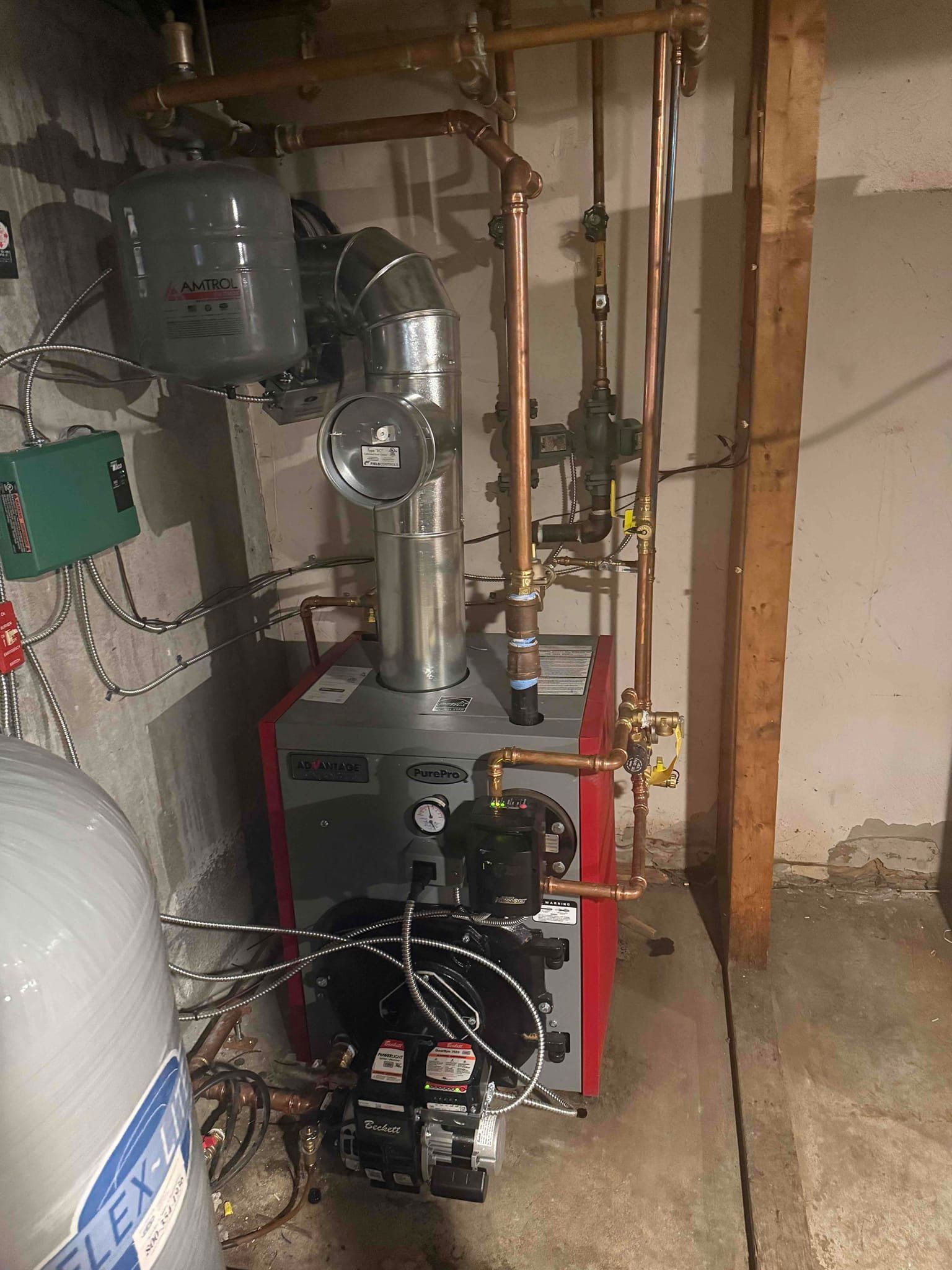 Red and gray boiler with copper pipes, connected to various tanks and equipment in a basement setting.