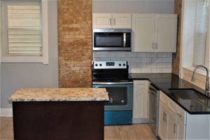 A kitchen with a stove , microwave , sink and cabinets.