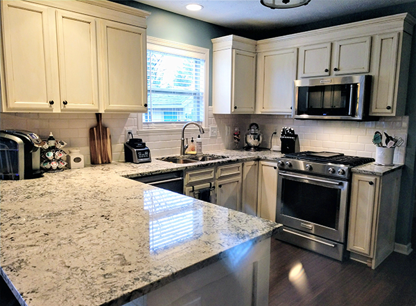 A kitchen with white cabinets , granite counter tops , stainless steel appliances and a window.