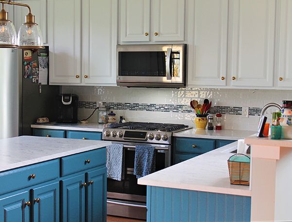 A kitchen with blue cabinets , white cabinets , a stove , a microwave , and a sink.