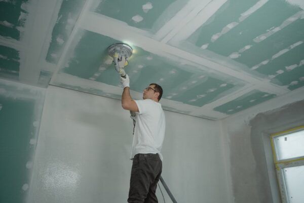 A man is sanding a ceiling with a sander.