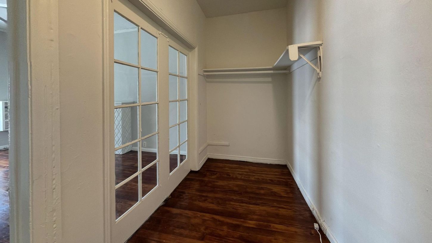 Hallway with french doors leading to a room with hardwood floors, closet on right with clothes rod.