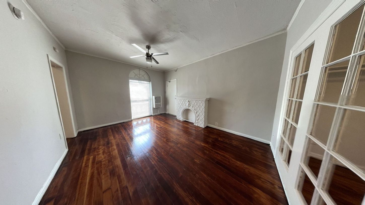 Empty room with glossy wood floors, gray walls, white fireplace and French doors.