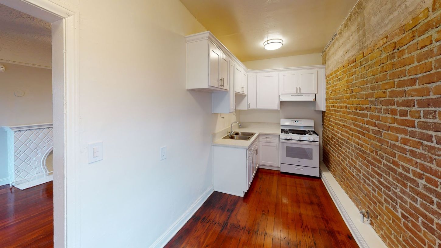 Small kitchen with white cabinets, exposed brick wall, and hardwood floor.